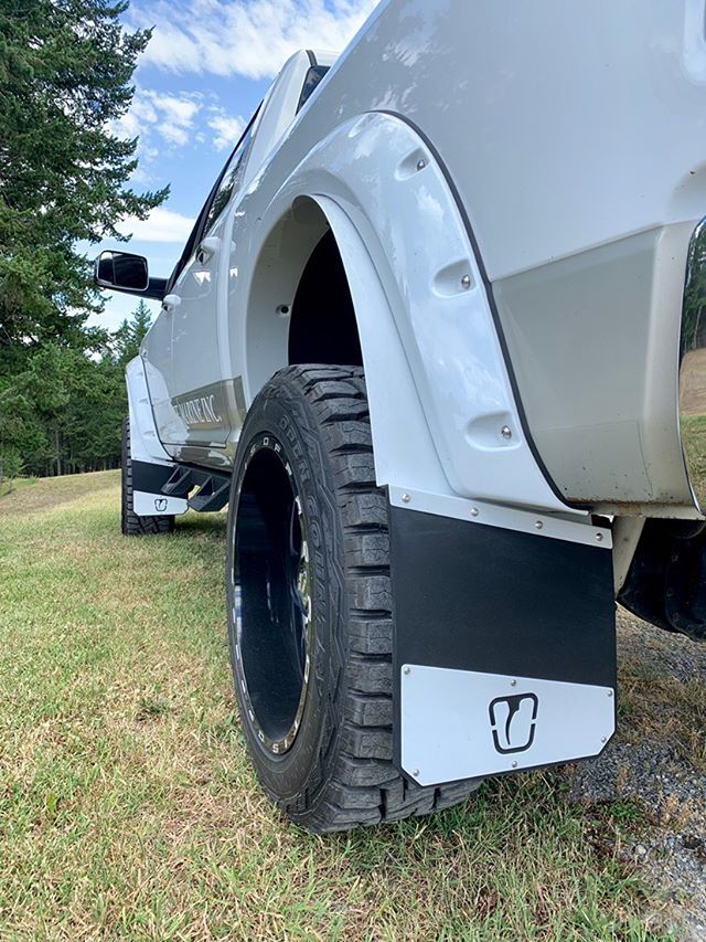 Close-up of a vehicle's tire with a mud flap on a grassy area with trees in the background
